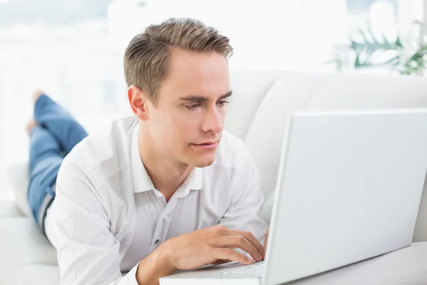 Avslappnad casual man använder laptop liggande på soffan — Stockfoto