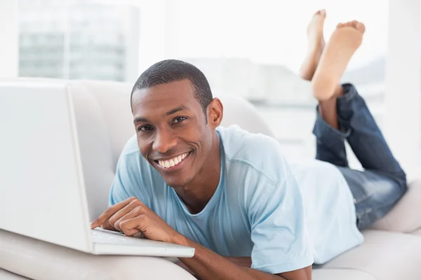 Ontspannen casual afro man met laptop liggend op de Bank — Stockfoto