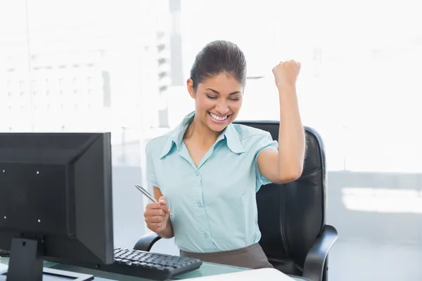 Happy businesswoman clenching fist at office desk — Stock Photo, Image