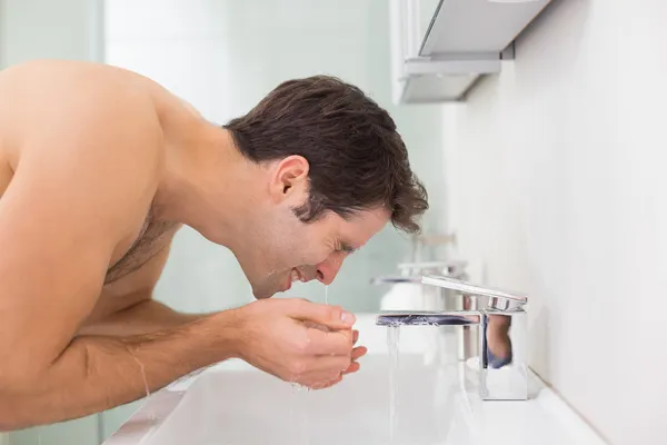 Vista lateral de la cara de lavado del hombre sin camisa en el baño —  Fotos de Stock