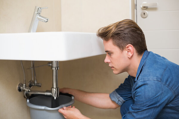 Handsome plumber repairing the drain of sink