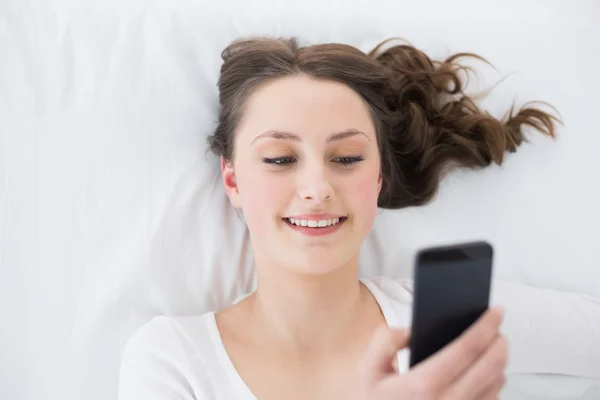 Junge Brünette mit Handy im Bett — Stockfoto