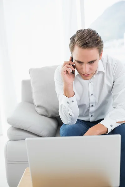 Casual young man using cellphone and laptop on sofa — Stock Photo, Image