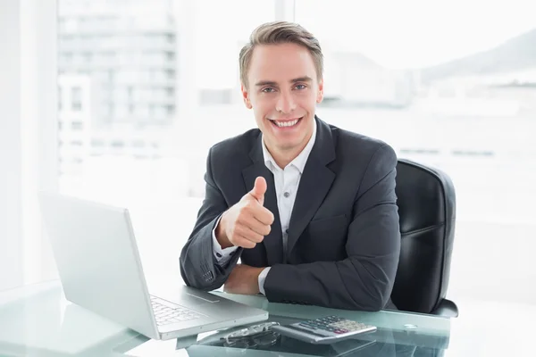Empresário com laptop gesticulando polegares na mesa do escritório Imagem De Stock
