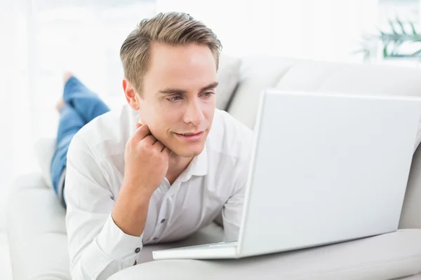 Relaxed casual man using laptop while lying on sofa — Stock Photo, Image