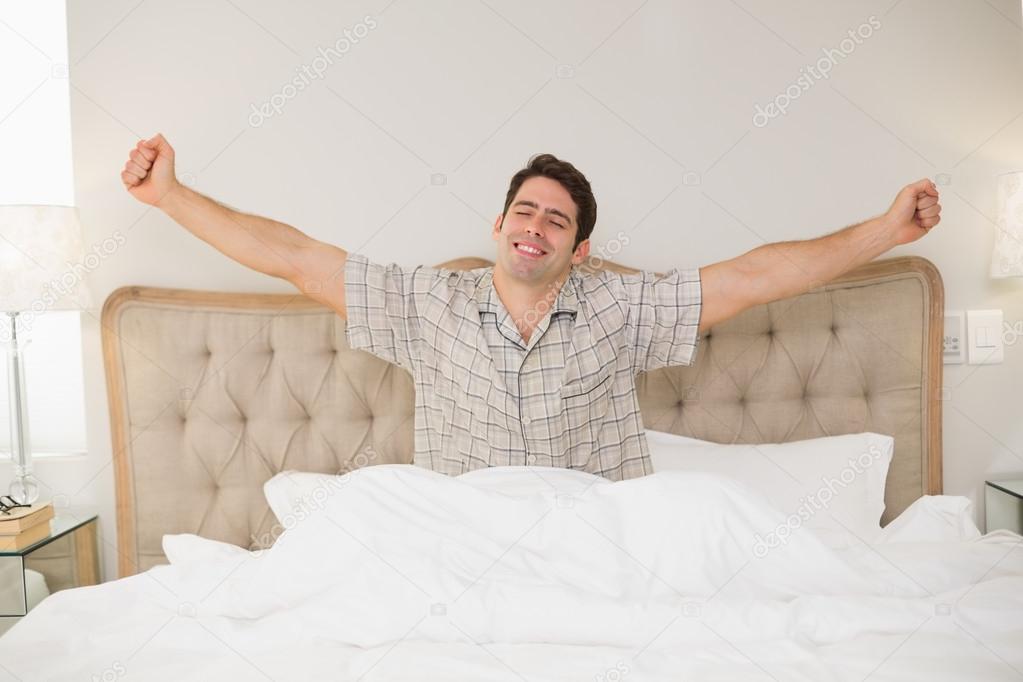 Young man waking up in bed and stretching his arms