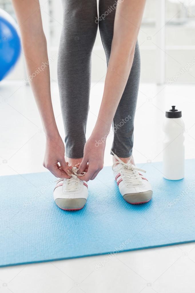 Low section of woman tying shoes with water bottle on floor