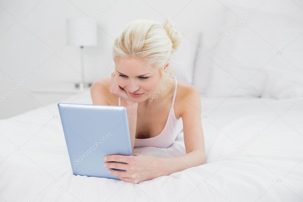 Content casual young blond using tablet PC in bed