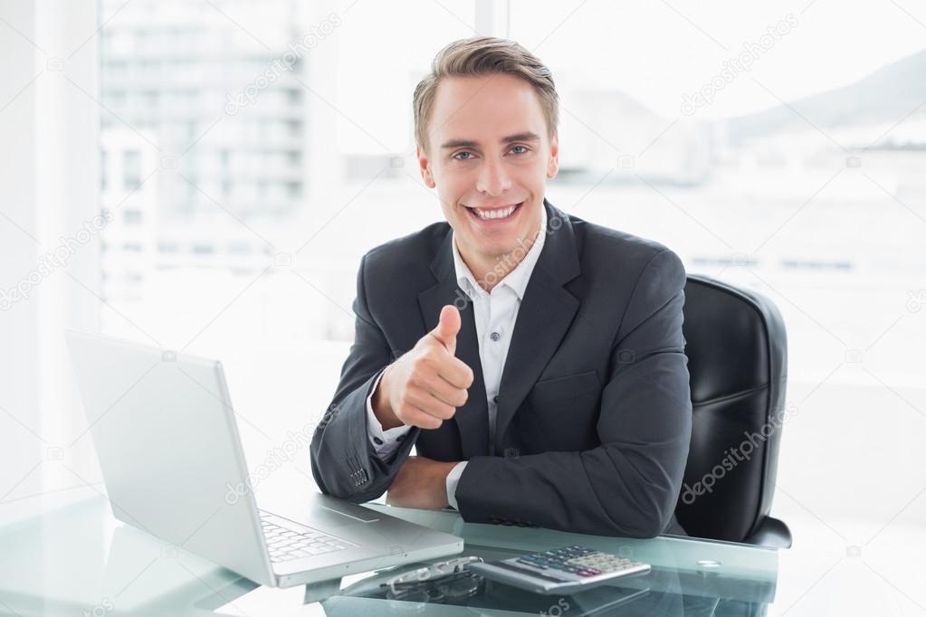 Businessman with laptop gesturing thumbs up at office desk
