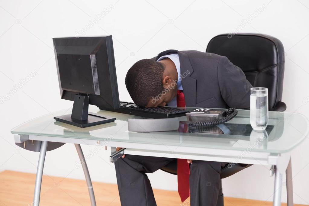 Afro businessman resting head on keyboard in office