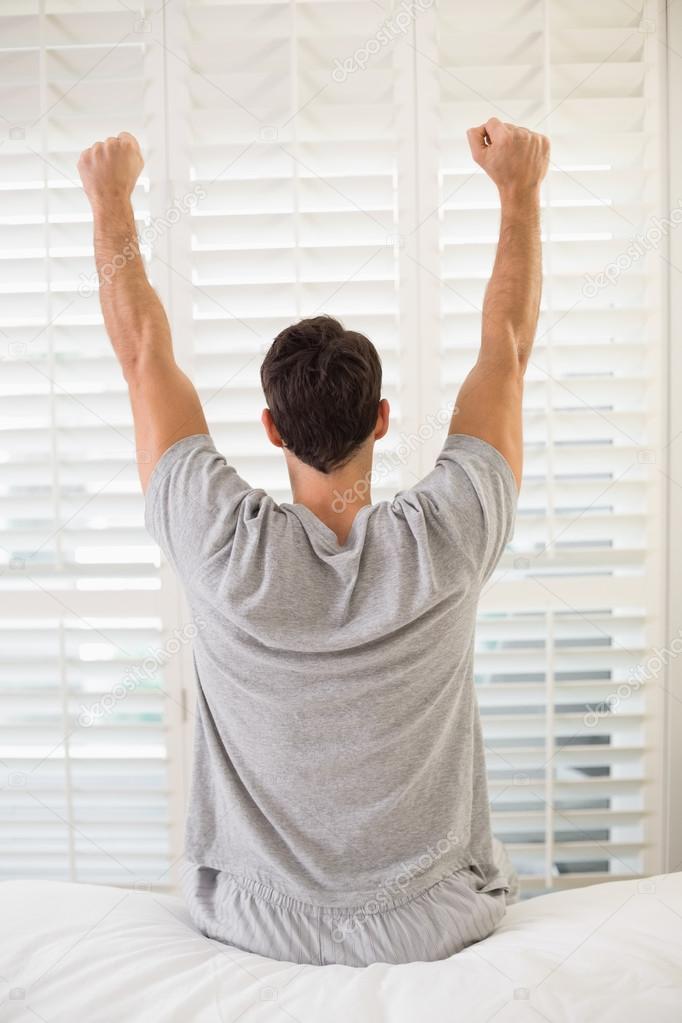 Rear view of man stretching his arms in bed