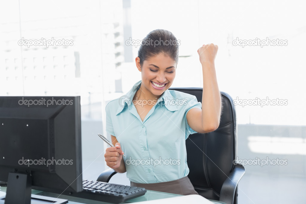 Happy businesswoman clenching fist at office desk