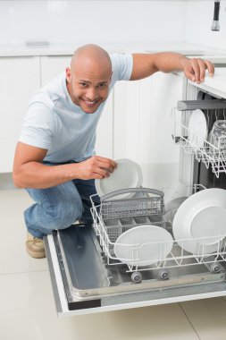 Mutfakta bulaşık makinesi kullanan gülümseyen adam portresi