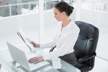 Gazete okuyan ve laptop kullanma office iş kadını