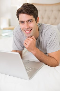 casual gülümseyen adam yatakta dizüstü kullanarak