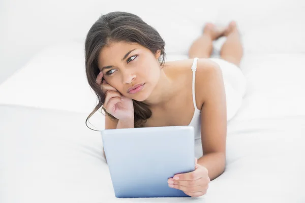 Mujer casual reflexivo usando tableta PC en la cama —  Fotos de Stock