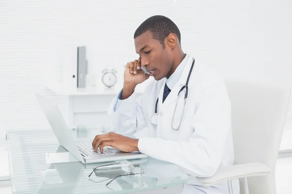 Концентрированный врач-мужчина с помощью мобильного телефона и ноутбука — стоковое фото