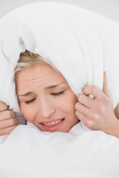 Displeased woman covering ears with pillow — Stock Photo, Image