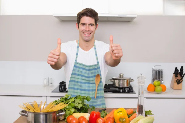 Smiling man with vegetables gesturing thumbs up in kitchen — Stock Photo, Image