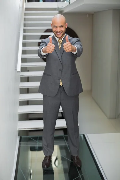 Elegant businessman gesturing thumbs up against staircase — Stock Photo, Image