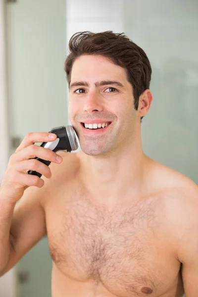 Sonriente hombre guapo sin camisa afeitándose con afeitadora eléctrica — Foto de Stock