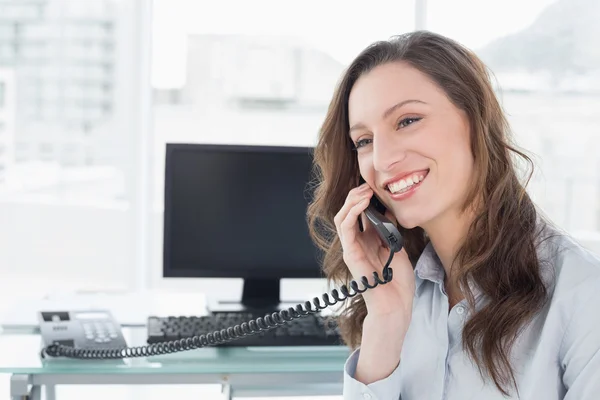 Femme d'affaires souriante utilisant le téléphone devant l'ordinateur — Photo