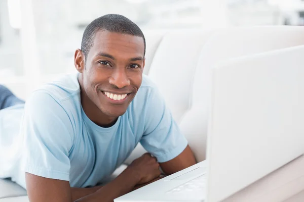 Ontspannen casual afro man met laptop liggend op de Bank — Stockfoto