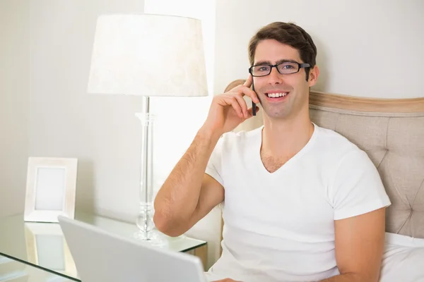 Casual sorrindo homem usando celular na cama — Fotografia de Stock