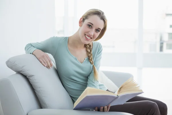 Fröhliche schöne Frau liest ein Buch, während sie auf der Couch sitzt — Stockfoto