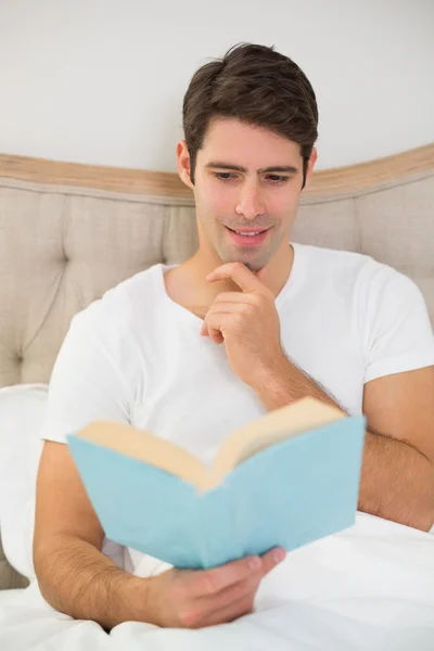 Relaxed young man reading book in bed — Stock Photo, Image