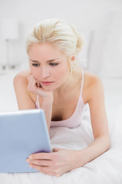 Zufriedene junge Blondine mit Tablet-PC im Bett — Stockfoto