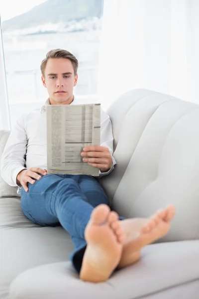 Volledige lengte van een ontspannen man leest de krant op sofa — Stockfoto