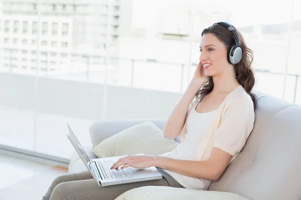 Casual vrouw laptop gebruikt terwijl u geniet van muziek op sofa — Stockfoto