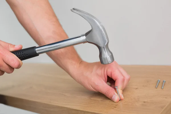 Hands hammering nail in wooden bench — Stock Photo, Image