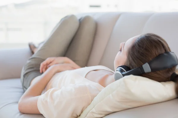 Расслабленная юная леди наслаждается музыкой на диване — стоковое фото