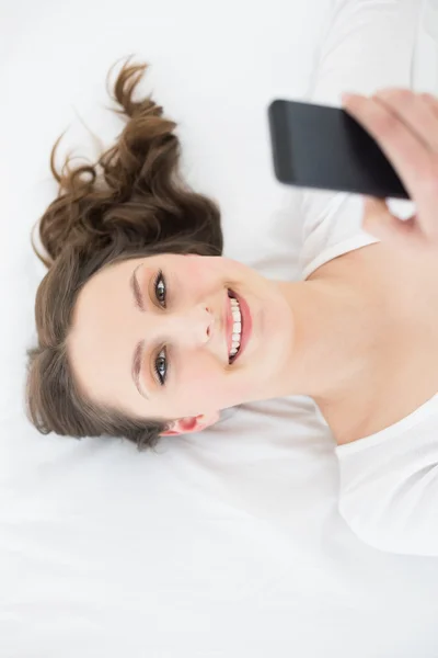 Junge Brünette mit Handy im Bett — Stockfoto