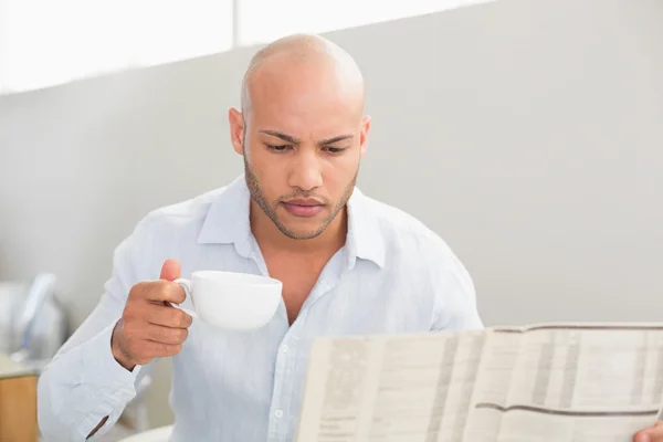 Mann trinkt Kaffee, während er zu Hause Zeitung liest — Stockfoto