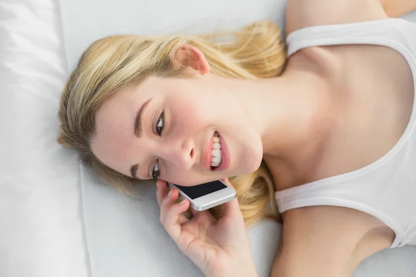 Mulher bonita telefonando com seu smartphone deitado em sua cama — Fotografia de Stock