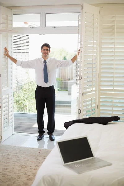 Smiling businessman by window at a hotel bedroom — Stock Photo, Image