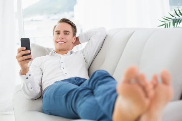 Avslappnad ung man liggande på soffan och textmeddelanden — Stockfoto