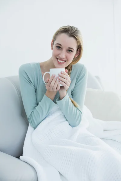 Natural young woman holding a cup sitting on couch — Stock Photo, Image