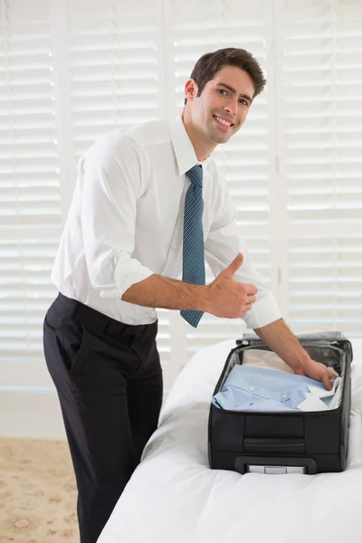 Smiling businessman unpacking luggage at a hotel bedroom — Stock Photo, Image