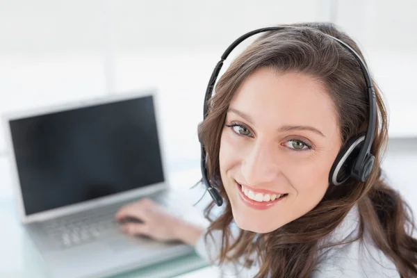 Smiling businesswoman wearing headset in front of laptop — Stock Photo, Image