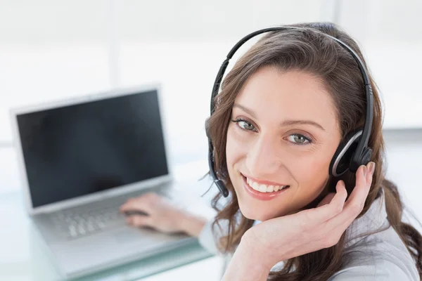 Femme d'affaires souriante portant un casque devant un ordinateur portable — Photo