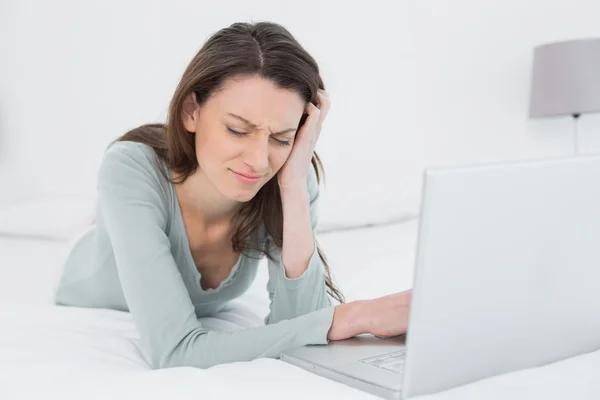 Traurige junge Frau mit Laptop im Bett liegend — Stockfoto