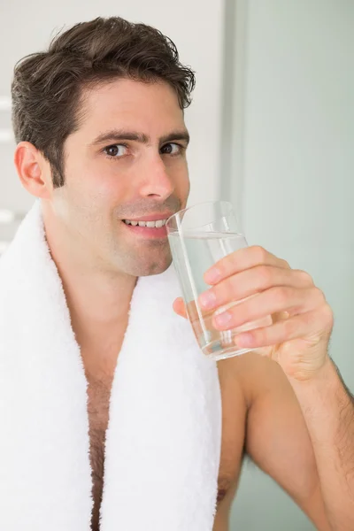 Мужчина пьет воду с полотенцем вокруг шеи дома — стоковое фото