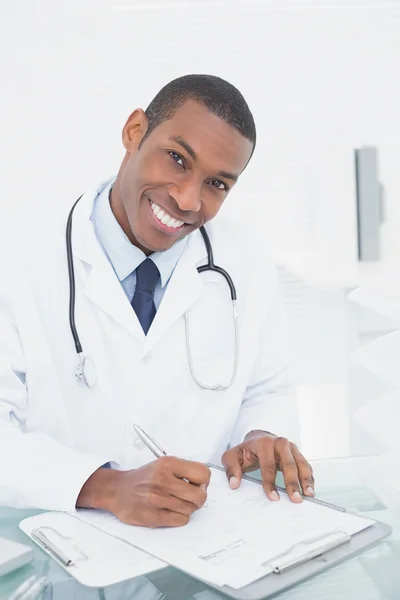 Médico sorridente escrevendo uma nota no consultório médico — Fotografia de Stock