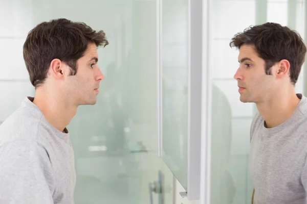 Widok z boku młody człowiek uśmiecha się do siebie w lustrze w łazience — Zdjęcie stockowe