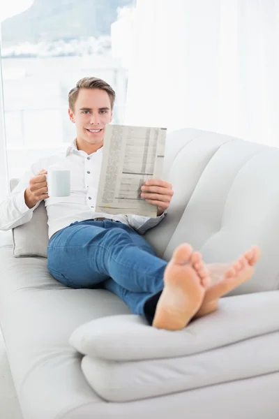 Avslappnad man dricka kaffe medan du läser tidningen på soffa — Stockfoto