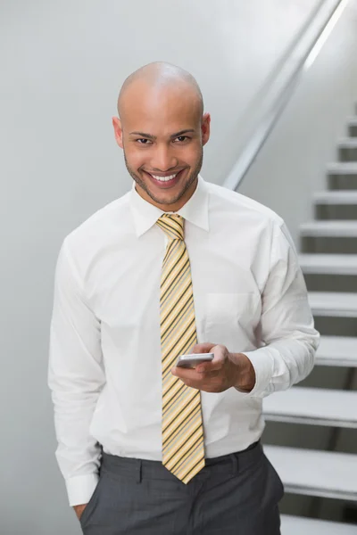 Smiling businessman text messaging against staircase — Stock Photo, Image